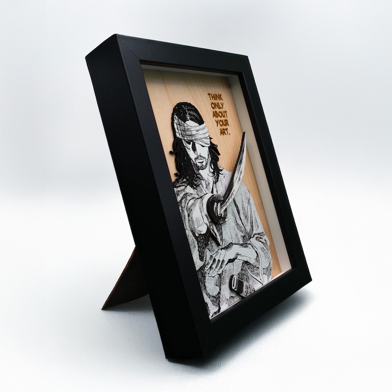May include: A black framed wood wall art piece with a black and white image of a blindfolded man holding a sword. The text "Think only about your art." is written in gold lettering on the wood.