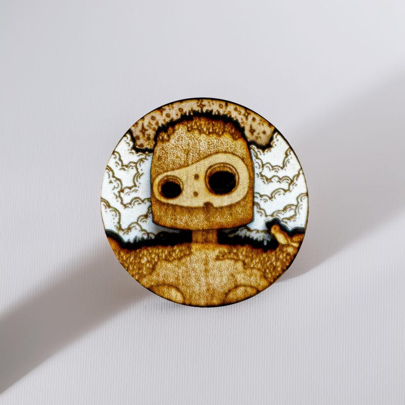 Round wooden magnet inspired by the guardian robot from Castle in the Sky. Handmade from layered plywood and MDF, it features a detailed engraving of the robot surrounded by clouds in warm golden and brown tones. Measures approximately 5 cm in diameter. A unique handmade piece perfect for Studio Ghibli collectors and anime enthusiasts.