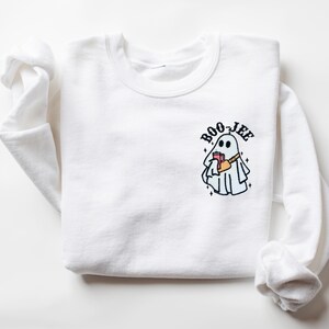 May include: White sweatshirt with a ghost holding a book and a cup of coffee. The ghost is wearing a bandana and the text "BOO-JEE" is above the ghost.