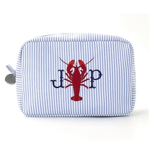 May include: A blue and white striped cosmetic bag with a red lobster design and the initials "J P" embroidered in navy blue. The bag has a zipper closure and a silver charm attached to the zipper pull.
