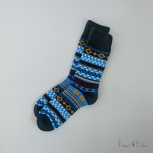 Op de afbeelding: Een paar blauwe en zwarte gepatroneerde sokken met een geometrisch ontwerp. De sokken hebben een donkerblauwe achtergrond met witte, oranje en rode accenten.