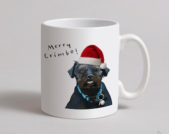 May include: White ceramic mug featuring a black dog wearing a red Santa hat and a blue collar. The mug has the text "Merry Crimbo!" and a signature at the bottom. A festive holiday gift.