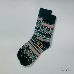 Op de afbeelding: Een paar donkergroene sokken met een geometrisch patroon in wit, grijs en oranje. De sokken zijn gevouwen en plat gelegd op een witte achtergrond.