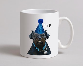 May include: White ceramic mug with a black dog wearing a blue party hat. The dog's name is "TED" printed on the mug.