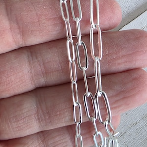 Pu&ograve; includere: Primo piano di tre fili di una catena d'argento con maglie ovali allungate. La catena &egrave; tenuta contro uno sfondo sfocato, mostrando la qualit&agrave; riflettente del metallo. Le maglie sono uniformi per dimensioni e forma, creando un'estetica elegante e moderna.