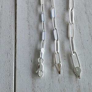Pu&ograve; includere: Primo piano di tre collane a catena d'argento con maglie ovali allungate. Ogni catena ha un diverso stile di chiusura. Una chiusura &egrave; a moschettone, le altre sono chiusure ad anello a molla. La parola "ITALY" &egrave; stampata su una chiusura.