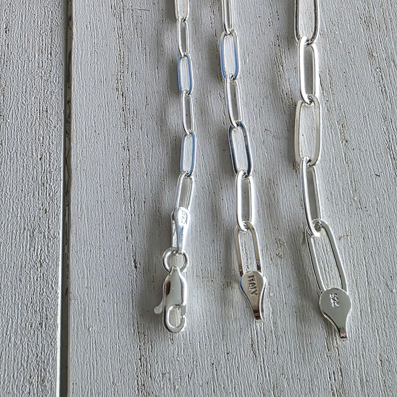 Pu&ograve; includere: Primo piano di tre collane a catena d'argento con maglie ovali allungate. Ogni catena ha un diverso stile di chiusura. Una chiusura &egrave; a moschettone, le altre sono chiusure ad anello a molla. La parola "ITALY" &egrave; stampata su una chiusura.