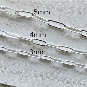 May include: Close-up of three silver chain samples with different link sizes: 3mm, 4mm, and 5mm. The chains are displayed against a light-colored, textured wooden surface. The sizes are labeled in black text.