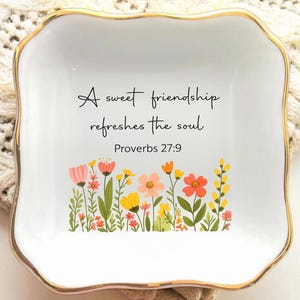 May include: A white ceramic trinket dish with a gold rim, featuring the quote "A sweet friendship refreshes the soul" and a floral design. The flowers are in shades of pink, yellow, and orange. Proverbs 27:9 is also printed on the dish.