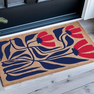 May include: A rectangular doormat with a floral design. The mat is made of a natural fiber material and features a pattern of red flowers and blue leaves. The doormat is placed in front of a black door.
