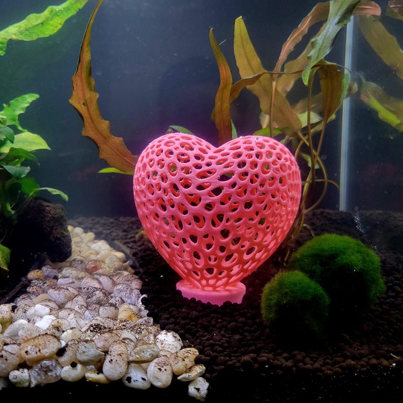 May include: A pink heart-shaped aquarium ornament with a lattice design. The ornament is made of a 3D printed material and has a small base.