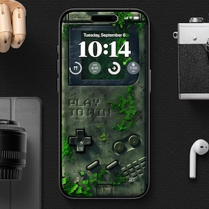 Puede incluir: Una funda de teléfono verde y gris con un diseño de consola de juegos retro. La funda tiene un reloj digital que marca las 10:14 y el texto "Play to Win".