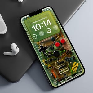 Puede incluir: Una funda transparente para teléfono con un diseño de Game Boy verde y negro. La pantalla del teléfono muestra la hora, "Martes, 6 de septiembre, 10:14".