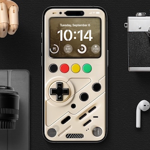 Puede incluir: Una funda de teléfono blanca y negra con un diseño de mando de videojuego retro. La pantalla del teléfono muestra un reloj digital con la hora 10:14 y la fecha martes 6 de septiembre.