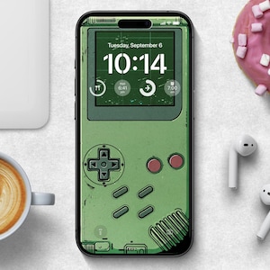 Puede incluir: Una funda de teléfono verde y negra con un diseño de consola de juegos retro. La funda presenta un reloj digital que muestra "10:14" y el texto "Martes, 6 de septiembre".