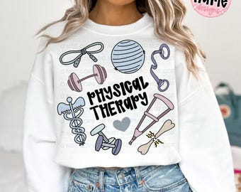 May include: White sweatshirt with a "PHYSICAL THERAPY" graphic. The design includes illustrations of exercise equipment, a medical symbol, and a heart. The sweatshirt has a crew neck and long sleeves.