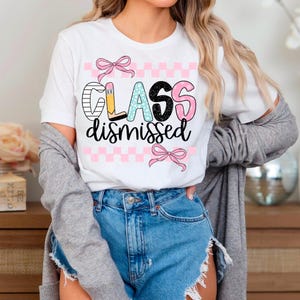 May include: White t-shirt with a pink and black checkered pattern and the text "Class dismissed" in colorful letters with a pink bow on each side.