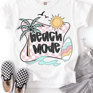 Puede incluir: Camiseta blanca con un dise&ntilde;o a cuadros rosa y blanco, una palmera, un sol, una tabla de surf y el texto "beach mode" en negro.