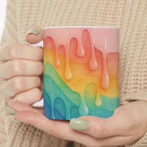 May include: A white ceramic mug with a rainbow drip design. The mug features a pink, orange, yellow, green, and blue color scheme. The design is abstract and resembles dripping paint.