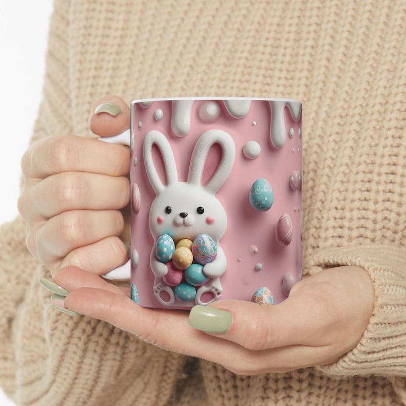 May include: A pink ceramic mug with a white bunny holding colorful Easter eggs. The bunny is surrounded by pink and white drizzled icing and colorful Easter eggs.