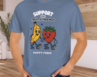 以下が含まれることがあります： 漫画のバナナとイチゴの上に「SUPPORT your FRUITY FRIENDS」という文字が書かれた水色のTシャツ。「HAPPY PRIDE」の文字が果物のキャラクターの下にあります。