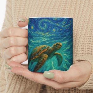 May include: White ceramic mug featuring a sea turtle swimming in a blue ocean with a starry sky background. The turtle has a brown and yellow shell. The mug is held in a person's hands.