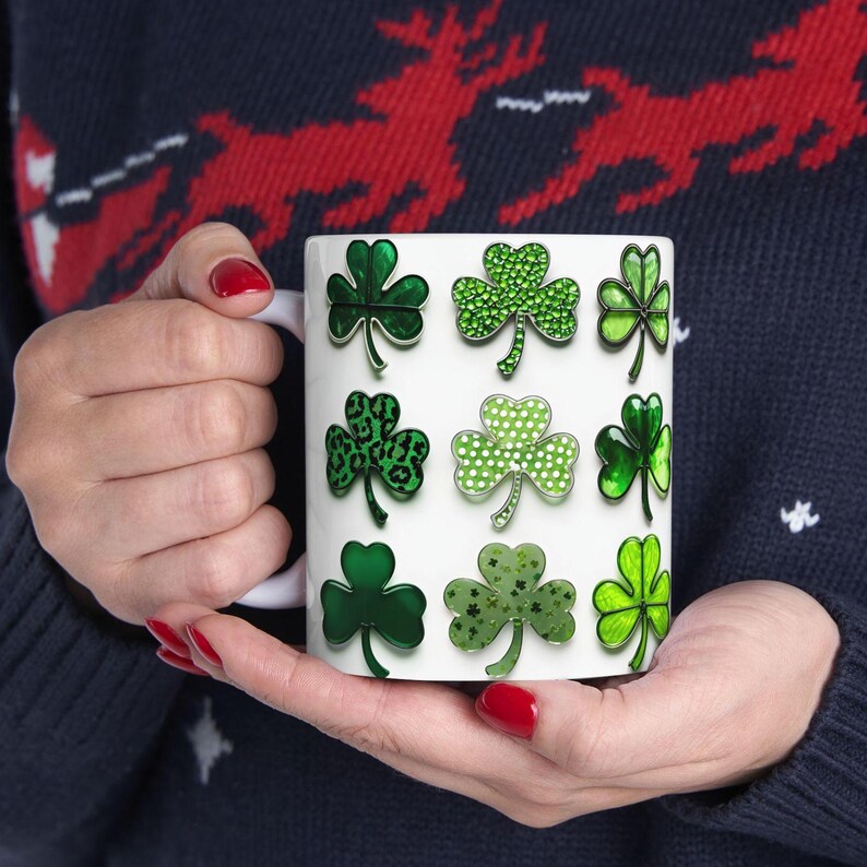 Pu&ograve; includere: Tazza in ceramica bianca con un design a trifoglio verde. I trifogli sono in vari stili, tra cui glitter, stampa leopardata e verde solido.