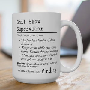 May include: White ceramic mug with the text "Shit Show Supervisor" and a definition. The mug also includes the name "Lindsey". A humorous gift for a supervisor or manager.