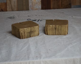 May include: Two wooden blocks painted gold, with a rough, rustic texture. The blocks are rectangular and have a slightly uneven surface.
