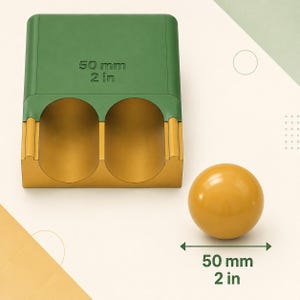 May include: A green and gold rectangular block with two cylindrical cutouts, labeled 50 mm 2 in, alongside a smooth gold sphere. A double-headed arrow indicates the sphere has a diameter of 50 mm 2 in, matching the size of the block's cutouts.