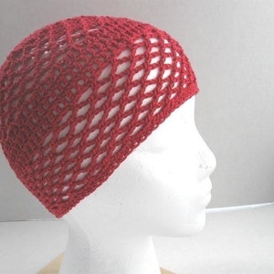 Peut inclure: Un bonnet en crochet rouge avec un motif en maille. Le bonnet est sur une tête de mannequin blanche.