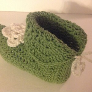 May include: Green crocheted slipper with white crocheted flower embellishments and a white crocheted tie.