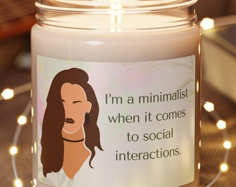 May include: A beige candle with a white label featuring a woman's illustration and the text "I'm a minimalist when it comes to social interactions."