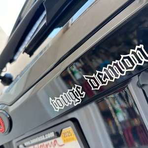 May include: A black car with a white "tongue demon" sticker on the back.