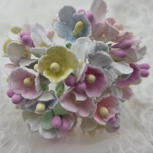 May include: A cluster of small, delicate paper flowers in pastel shades of pink, yellow, blue, and white. The flowers are arranged in a bouquet-like shape.