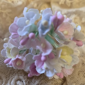 May include: A cluster of pastel-colored artificial flowers. The arrangement features white, pink, yellow, and light blue blossoms with small, round, light-colored centers. The stems are green, and the overall effect is delicate and soft.