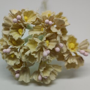 May include: A cluster of small, cream-colored paper flowers with pink centers. The flowers are arranged in a bouquet and have a delicate, vintage look.