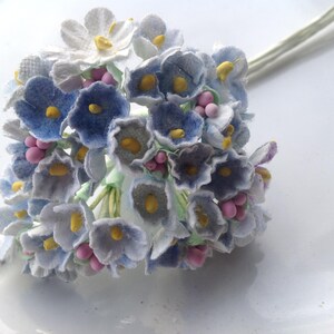 May include: A bouquet of blue and white fabric flowers with pink centers. The flowers are arranged in a cluster and have a vintage look.