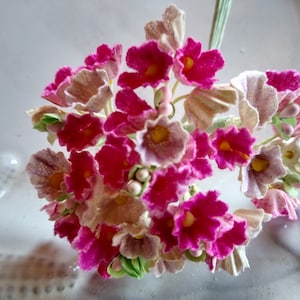 May include: A cluster of pink and white fabric flowers, resembling a bouquet. The flowers are delicate and have a vintage aesthetic.