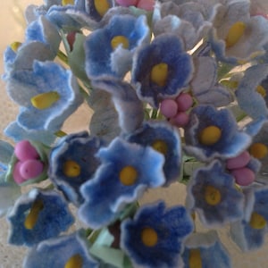 May include: A bouquet of blue and white felt flowers with yellow centers and pink accents. The flowers are arranged in a cluster and have a soft, fuzzy texture.