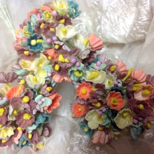 May include: A bouquet of small, delicate fabric flowers in shades of pink, yellow, green, and brown. The flowers are arranged in a cluster and have a vintage aesthetic.