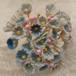 May include: A cluster of blue and white artificial flowers with pink centers. The flowers are arranged in a bouquet shape and have a vintage look.