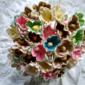 May include: A bouquet of small, fabric flowers in various colors, including brown, pink, yellow, blue, and green. The flowers are clustered together and have a vintage aesthetic.