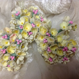 May include: A bouquet of delicate, pale yellow paper flowers with pink accents. The flowers are arranged in a cluster and have a vintage aesthetic.