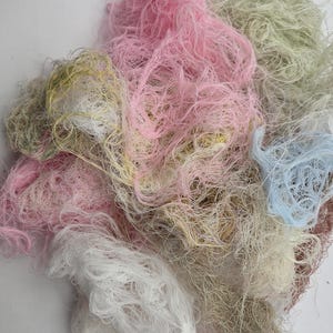 May include: A pile of colorful yarn in shades of pink, white, beige, green, and blue. The yarn is loosely spun and appears soft, with a tangled texture. Ideal for crafting projects like knitting or crochet.