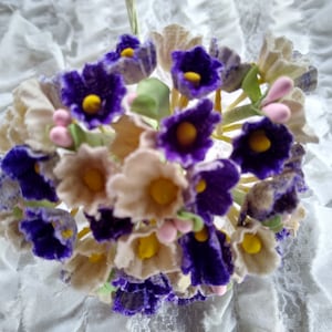 May include: A bouquet of artificial flowers with purple and white blossoms. The flowers are arranged in a circular shape and have a vintage aesthetic.