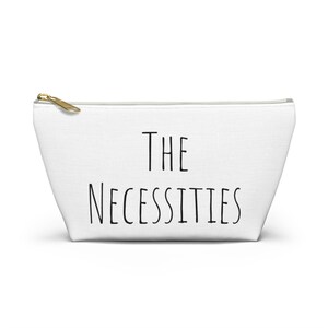 May include: White canvas zippered pouch with the text "THE NECESSITIES" printed in black.