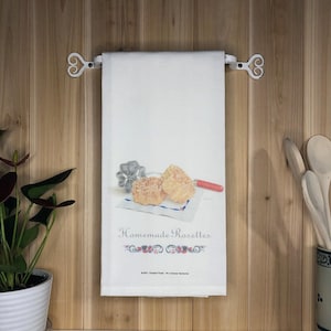 May include: A white kitchen towel with a red, white, and blue design. The towel features an illustration of two homemade rosettes, a rosette mold, and a red spatula. The text "Homemade Rosettes" is printed on the towel.