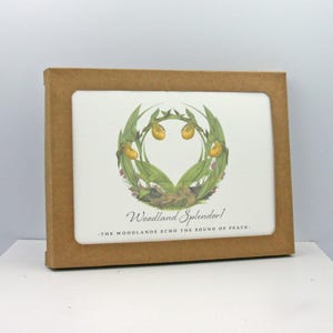 May include: A rectangular card with a floral illustration of yellow and green flowers and leaves, framed in a brown cardboard box. The text "Woodland Splendor!" and "- THE WOODLANDS ECHO THE SOUND OF PEACE -" are visible.