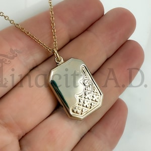 May include: A gold-coloured rectangular pendant necklace with an ornate design on the lower right corner. The pendant hangs from a delicate gold chain. The pendant has a shiny, reflective surface.